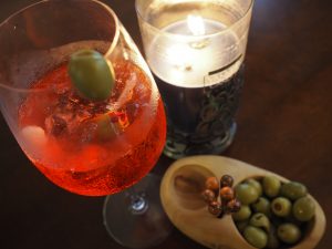 A spritz on the table with a candle and bowl of olives