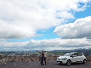 Tucker, Caitlin, and their car overlooking the Irish countryside on their road trip adventure