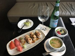 A sushi plate, miso soup, fruit, and sparkling water.