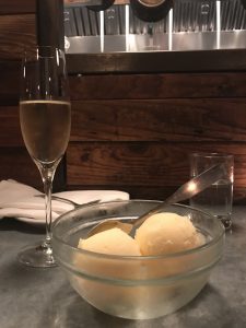 A bowl of sorbet with a glass of Cava in the background.