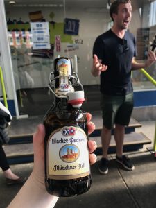 Hand holding a bottle of beer with a happy person in the background.