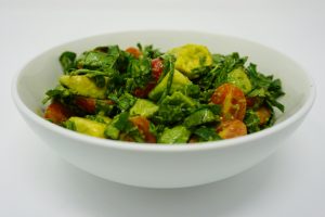 White bowl with tomatoes, spinach, and avocado.