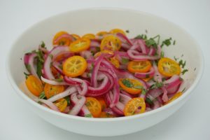 White bowl with pickled red onion, sliced kumquat, and cilantro.