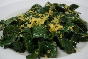 White plate with sauteed kale and lemon zest.