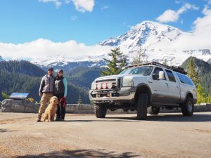 Two adults, a dog, and a truck in front of Mt. Rainier.