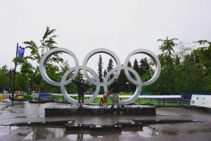 Two adults and a dog posing in front of the Whistler Olympic Rings.