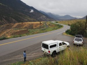 Two trucks pulled over on the highway with mountain views in the background.