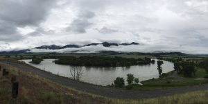 A bend in the Yellowstone River surrounded by clouds and mountains.