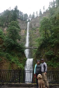 Two adults and a cute dog posing in front of Multnomah Falls.