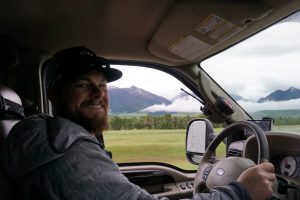 Tucker driving with clouds and mountains in the background.