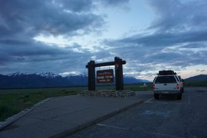 A truck parked next to the Grand Tetons National Park sign with mountains in the background.