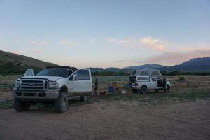 Two trucks parked in a field during sunset.