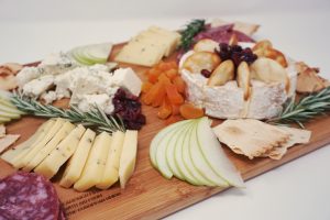 A wooden board with cheese and accompaniments.