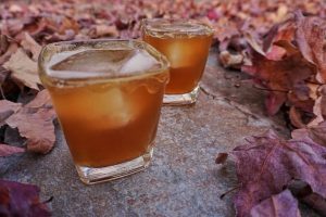 Two glasses of Spiced Whiskey Ginger with honey dripping off the sides