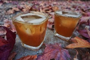 Two glasses of Spiced Whiskey Ginger surrounded by fall leaves