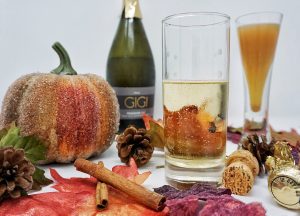 A glass of champagne and a glass of apple cider surrounded by fall decor