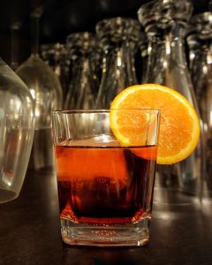 A glass with a red Negroni cocktail garnished with an orange slice.