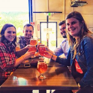 Four people around a table cheers-ing beers.