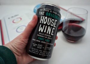 Can of house wine with a glass of pinot noir in the background.