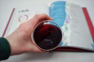 Caitlin holding a glass of canned Pinot Noir in front of the Wine Folly book.