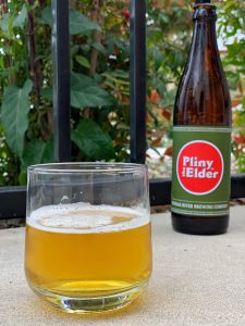 Glass of Pliny the Elder beer with bottle in the background.