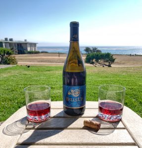 Bottle of Bells Up Titan Pinot Noir, an Oregon wine from the Willamette Valley, with two glasses and an ocean view in the background.