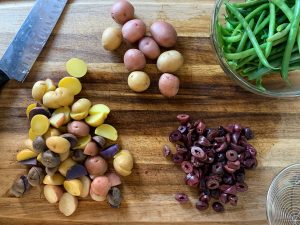 Cutting board with potatoes, olives, and green beans for the salad